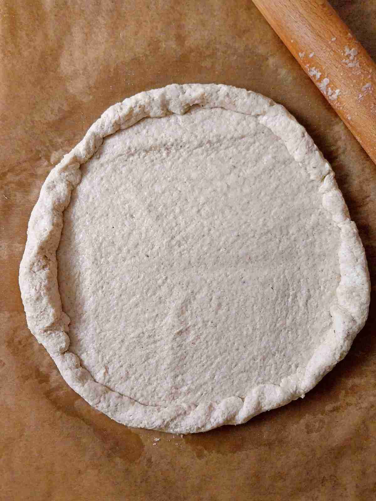 Sourdough pizza crust shaped into a circle on parchment paper.