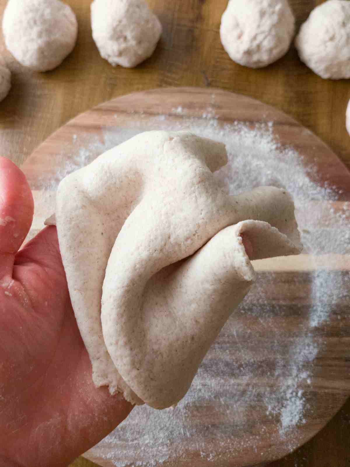 Rolled out flatbread dough held by a hand.