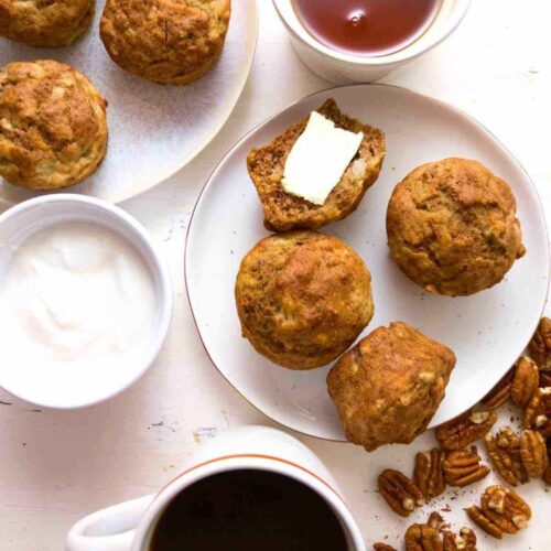 Muffins on a plate with coffee and maple syrup in the background.