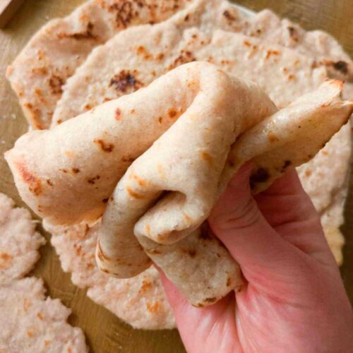 Gluten-free sourdough flatbread bent and held by a hand.