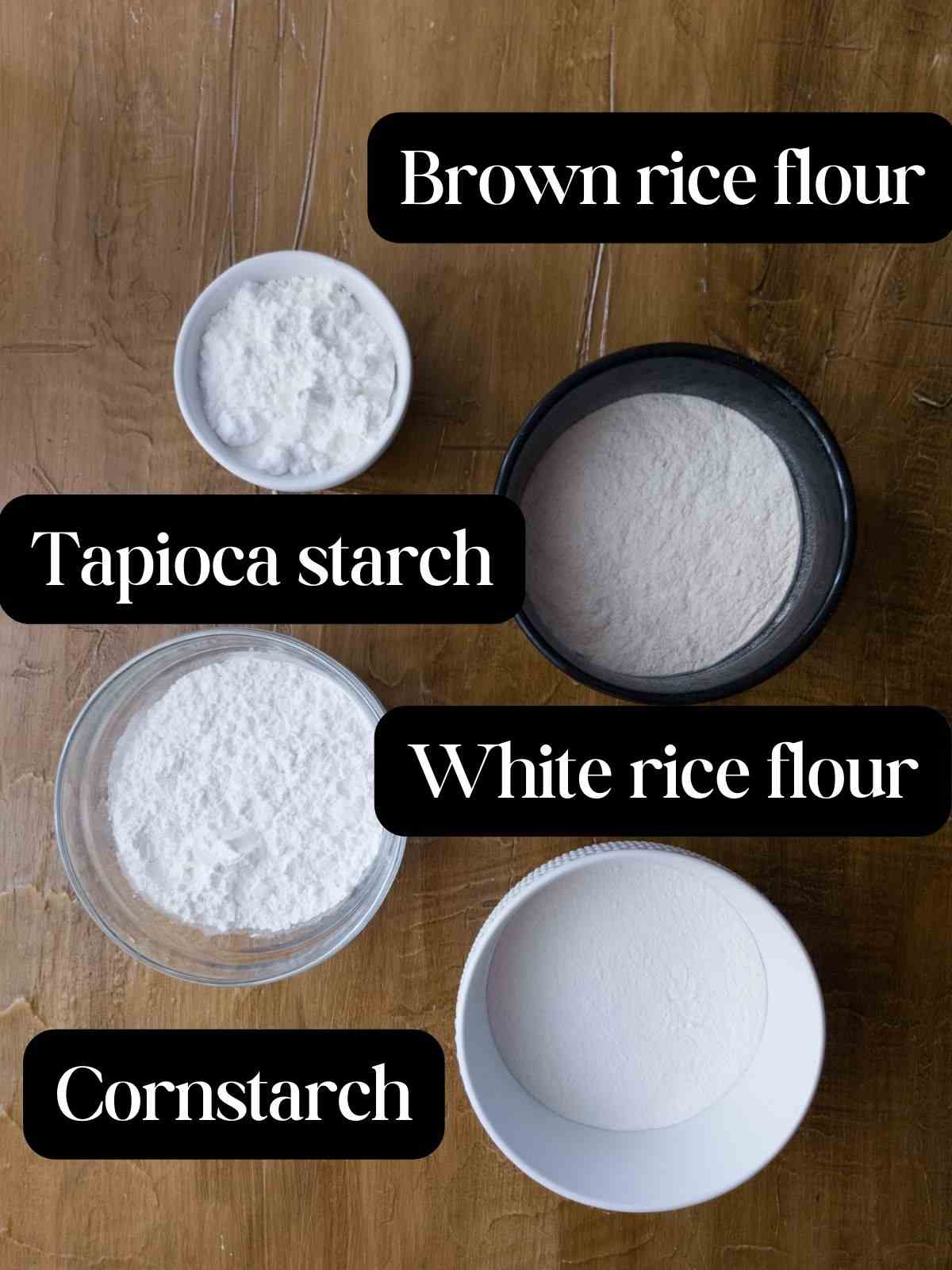 Different GF flours in bowls on a wooden surface.