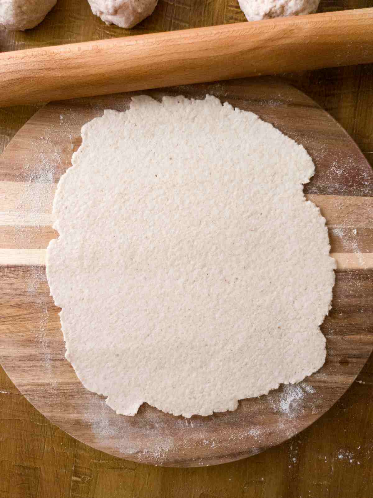 One flatbread rolled out on a cutting board with the rolling pin above it.