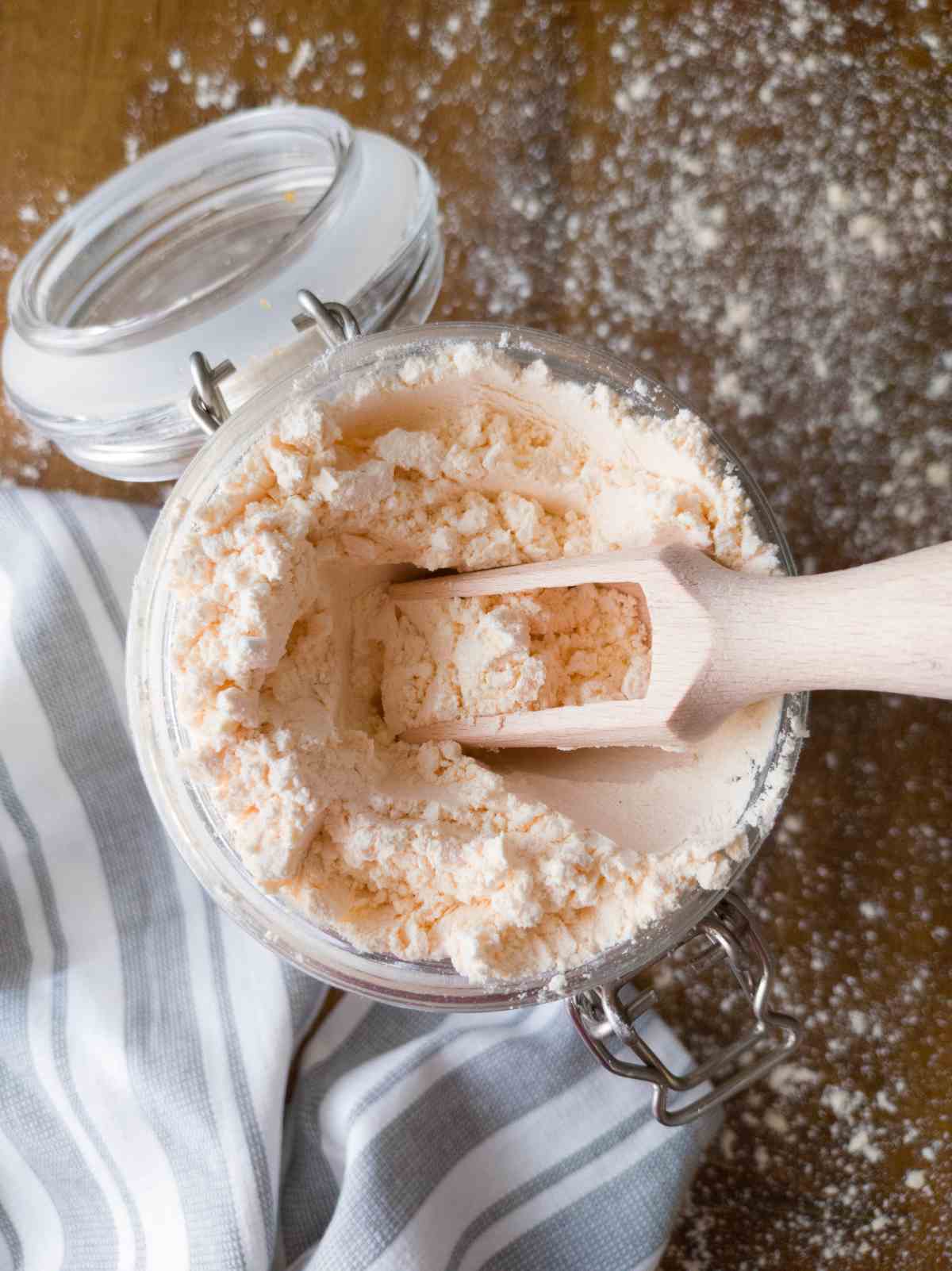 Gluten-free rice-free flour in a large jar with a wooden measuring spoon and a kitchen towel on the side.