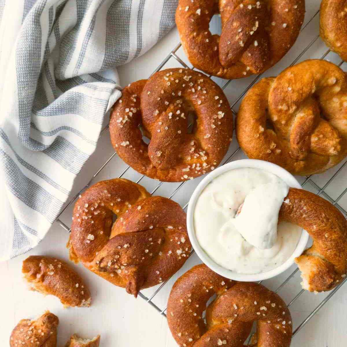 Gluten-free sourdough soft pretzels on a cooling rack with a tea towel and cheese sauce.