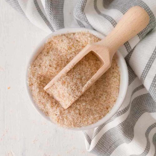 Psyllium husk in a small white bowl with a small wooden spoon in it.