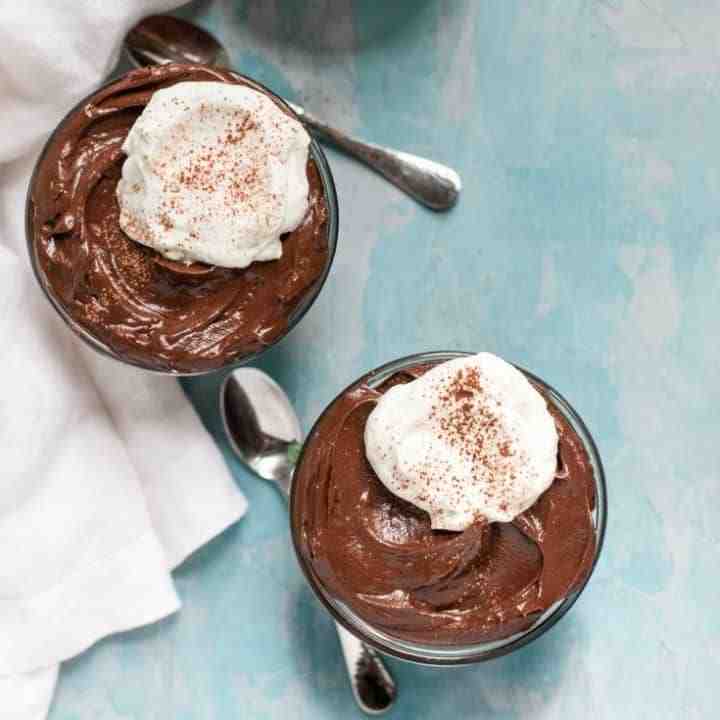 Chocolate avocado mousse in two cups with spoons in the background.