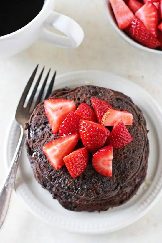 Chocolate buckwheat pancakes with strawberries on a plate with a fork on the side.