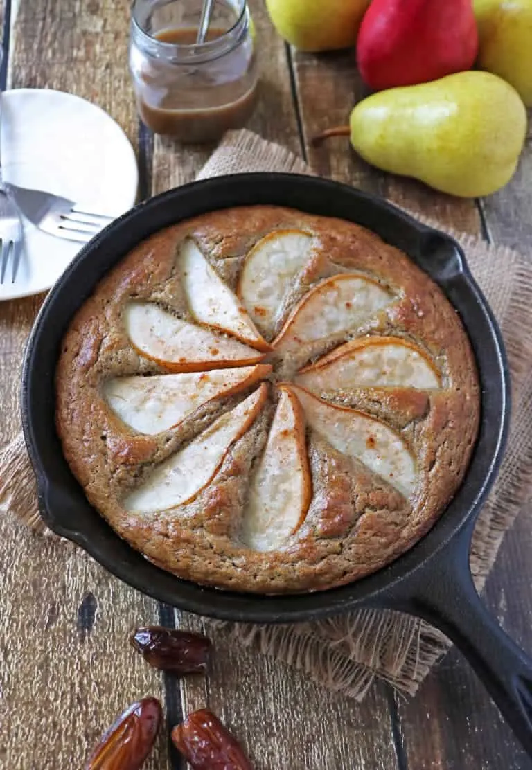 Gluten-free pear date skillet cake in a cast iron skillet on a table with fruits.