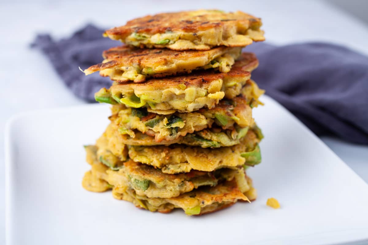 Veggie Fritters stacked on a white plate with a tea towel in the background.