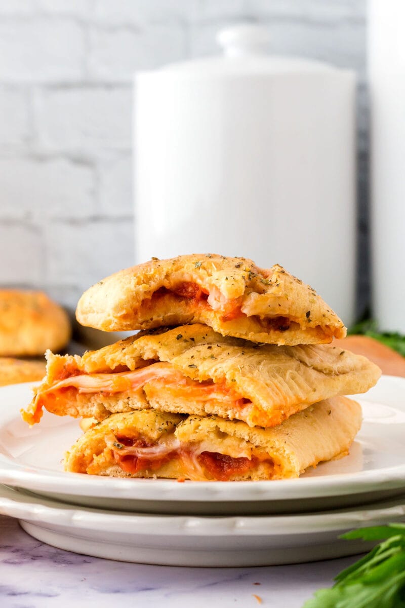 homemade hot pockets stacked on two plates with a white wall in the background.