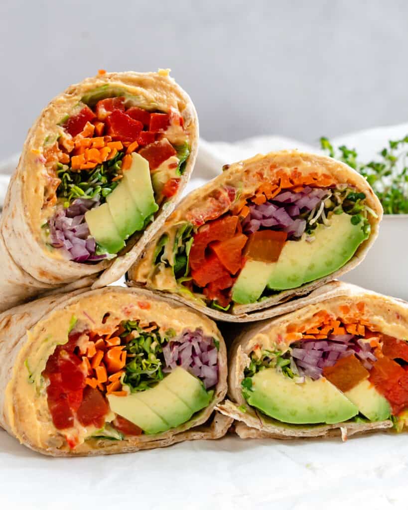 Hummus tortilla wraps cut in halves stacked on a white kitchen table.