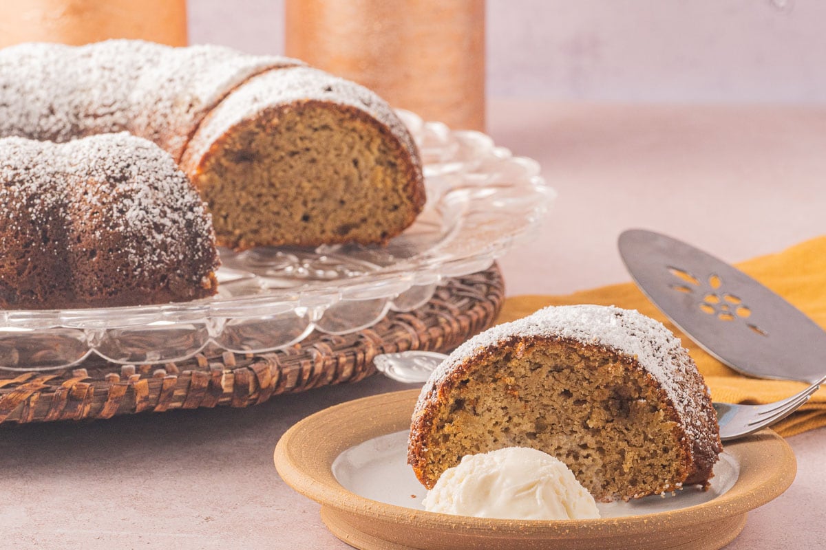 Sugar free apple cake slice on a plate with the rest of the cake in the background.