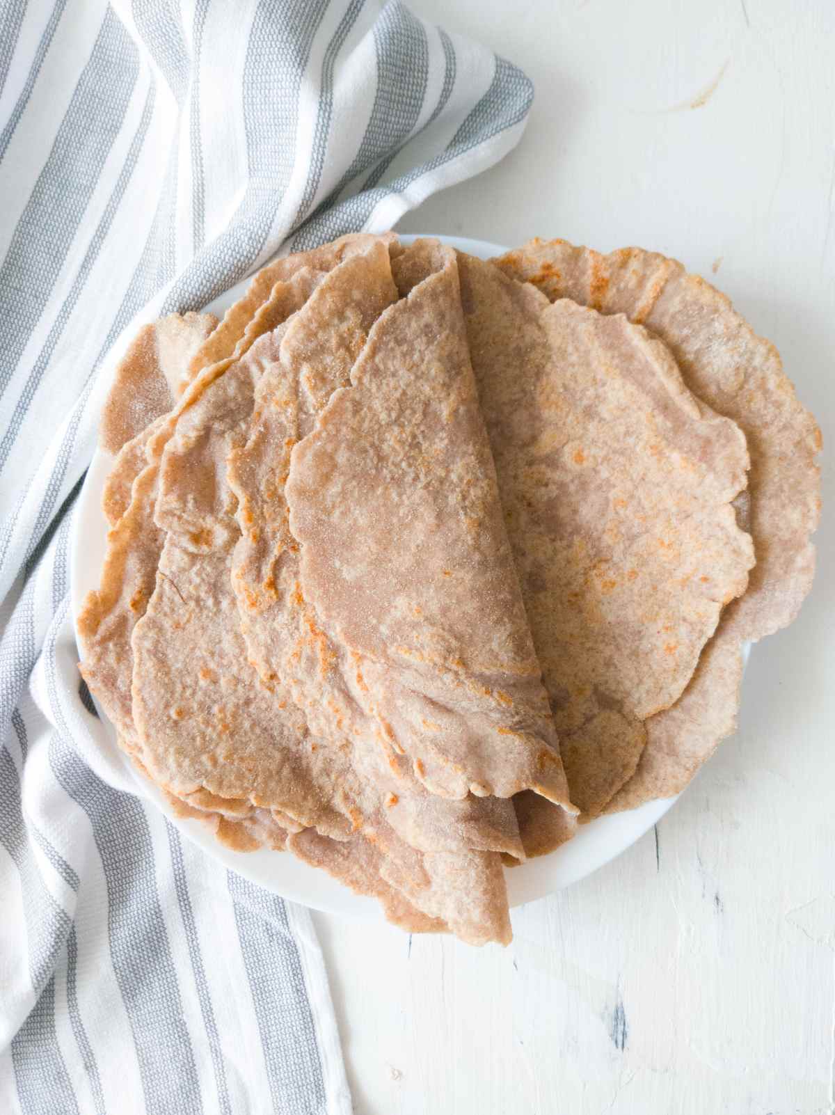 Buckwheat tortilla wraps on a plate against a white surface with a kitchen towel.