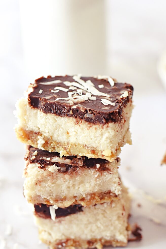 No-bake coconut bars stack on a white table.