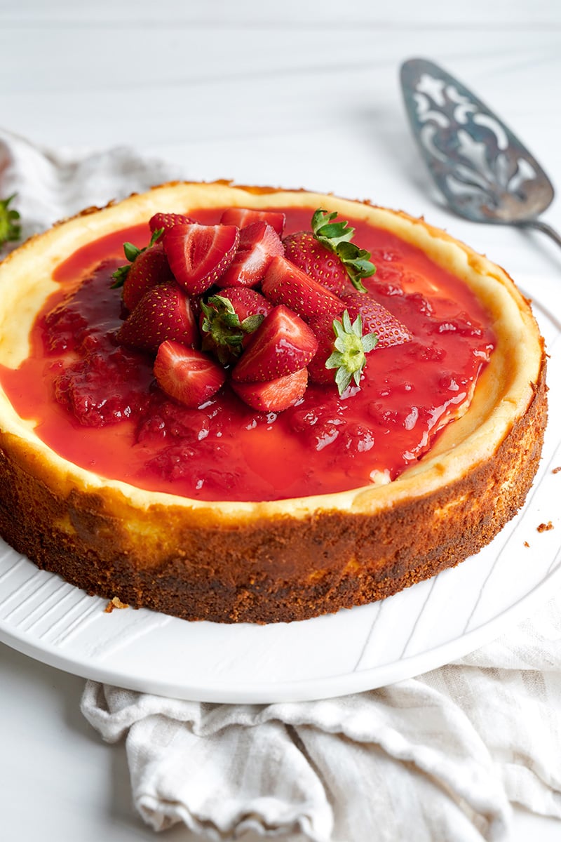 French cheesecake with strawberries on the top with a spatula in the background.