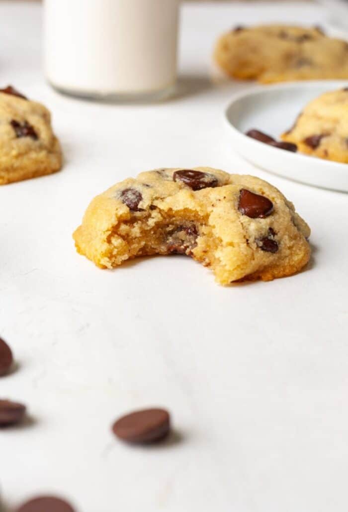 A chocolate chip cookies bit on a table with milk in the background.