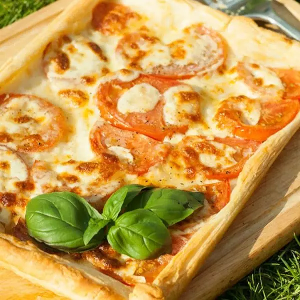Italian puff pastry tart with fresh basil on a wooden surface.