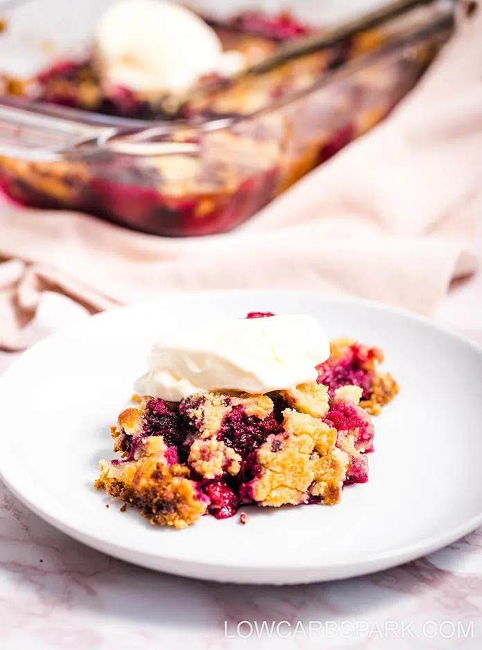 Berry dump cake on a white plate with the baking dish in the background. 