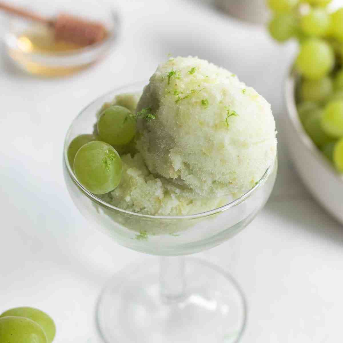 Ice cream in a glass bowl with grapes on the side.