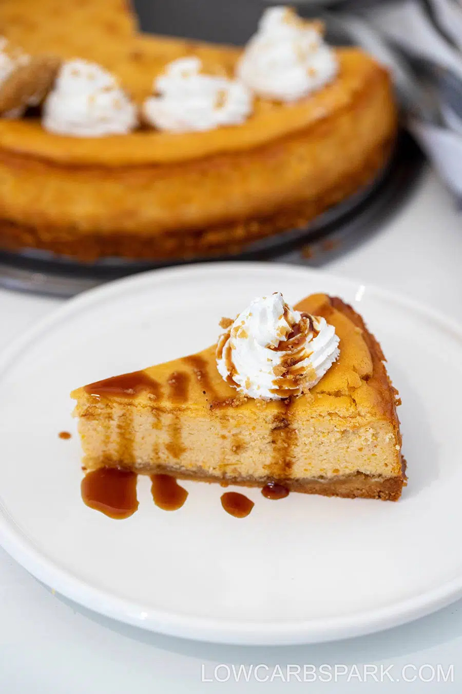 Pumpkin cheesecake slice on a white plate with the rest of the cheesecake in the background.