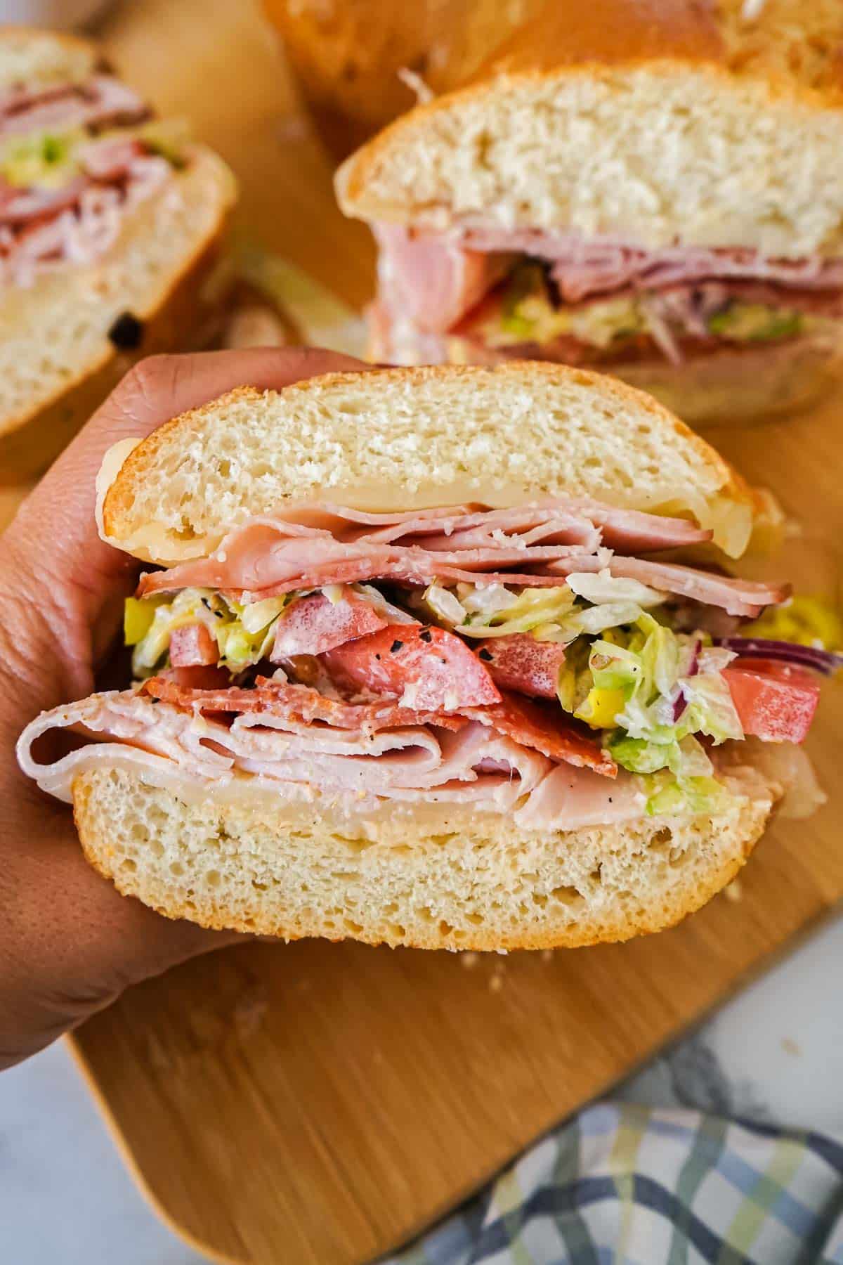 Italian grinder sandwich recipe held by a hand with a wooden board in the background.