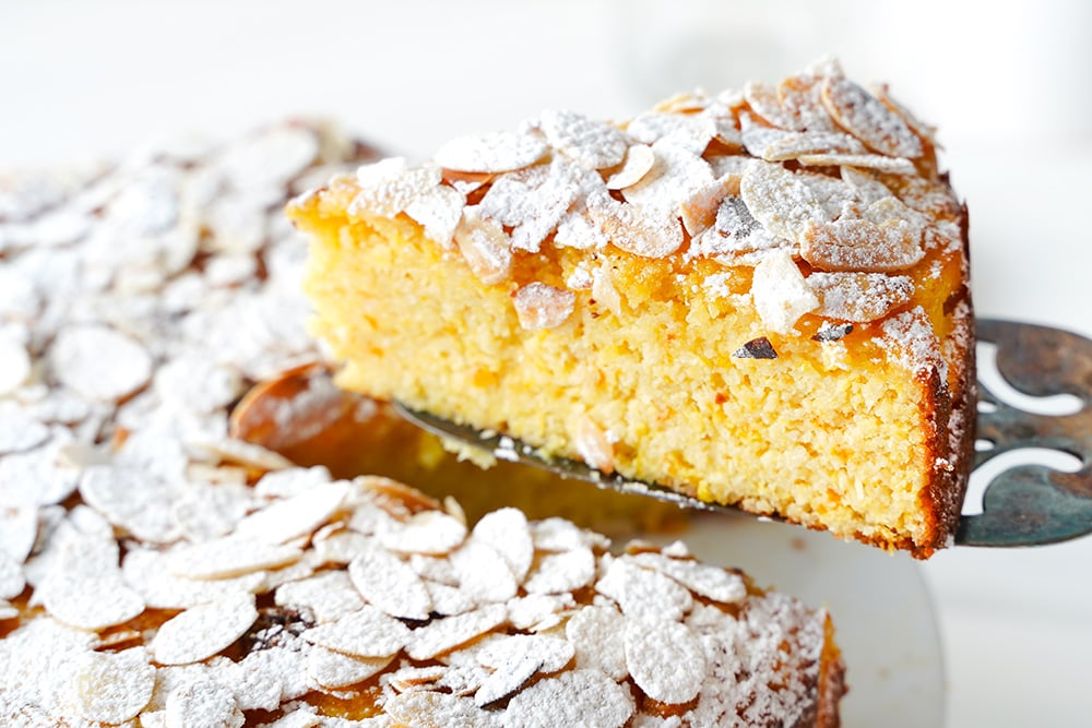 A slice of the almond orange cake being lifted from the rest of the cake with a spatula.