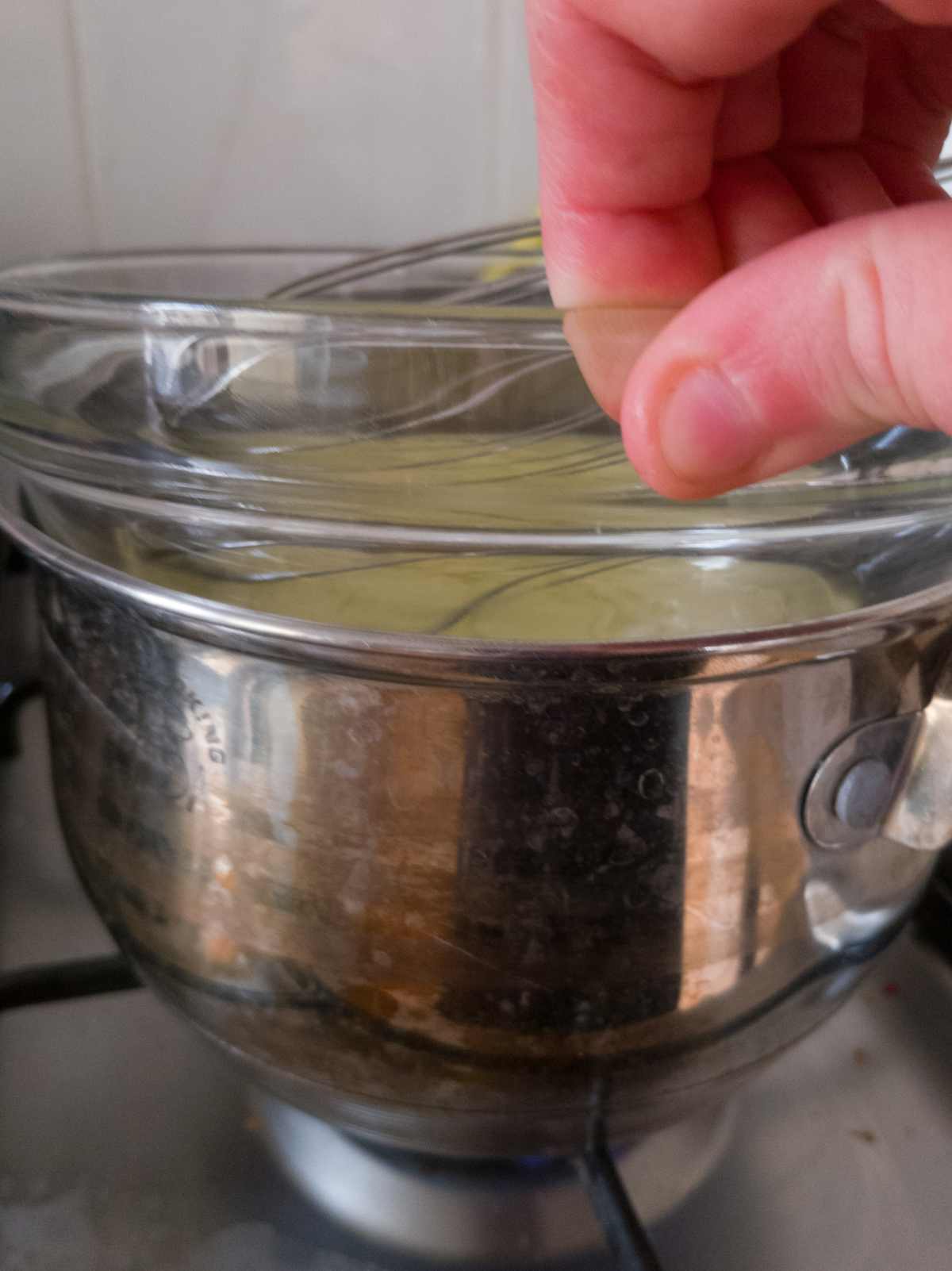 Placing the glass bowl with egg whites over a metal saucepan on the stove.