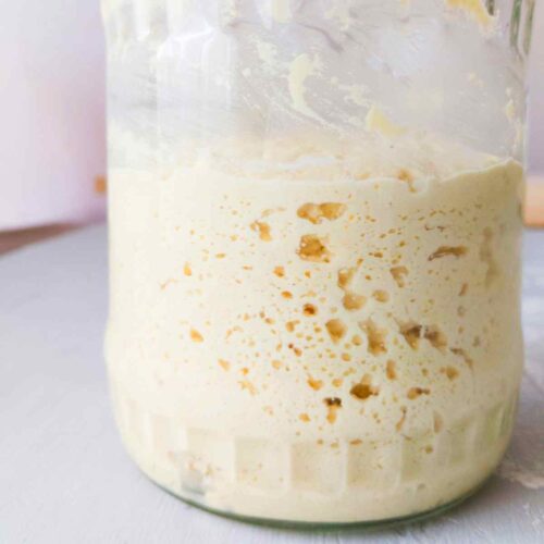 A glass jar with sourdough starter in it filled with air pockets.
