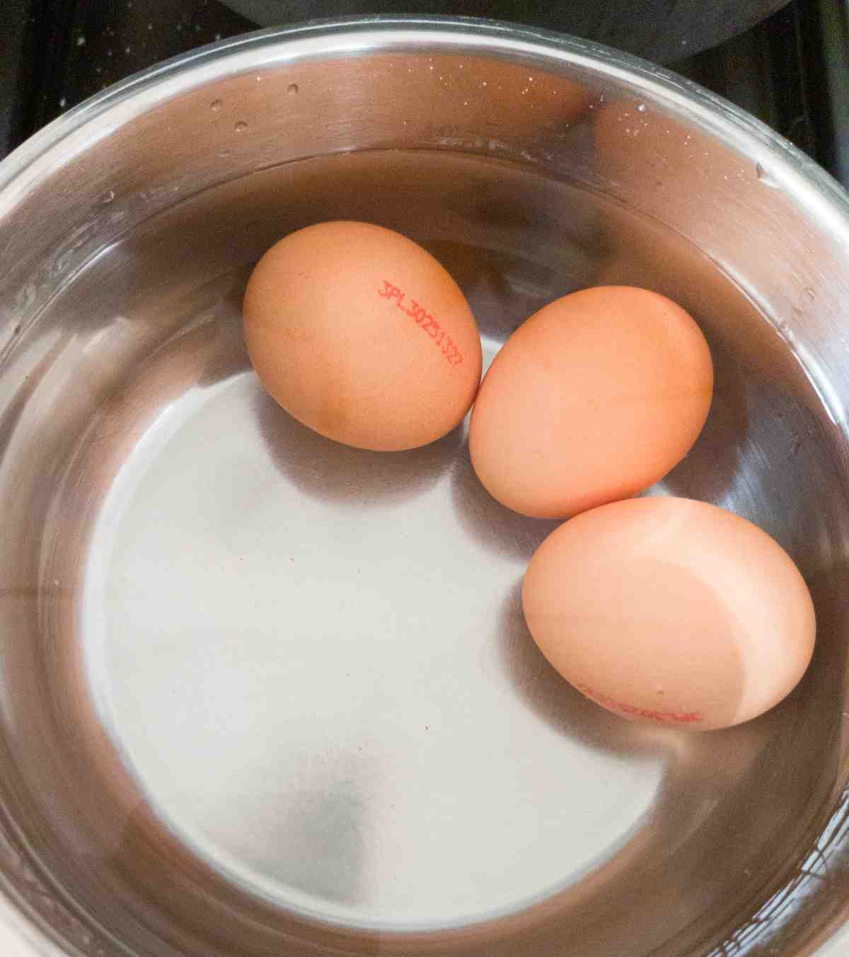 Three eggs in a small saucepan filled with water.