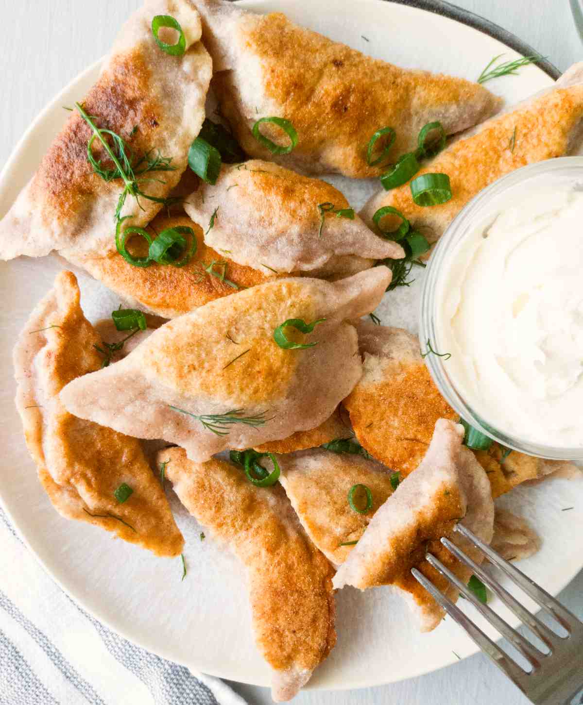 Finidhed gluten-free pierogies on a plate with a fork next to it and a white sauce on the side.