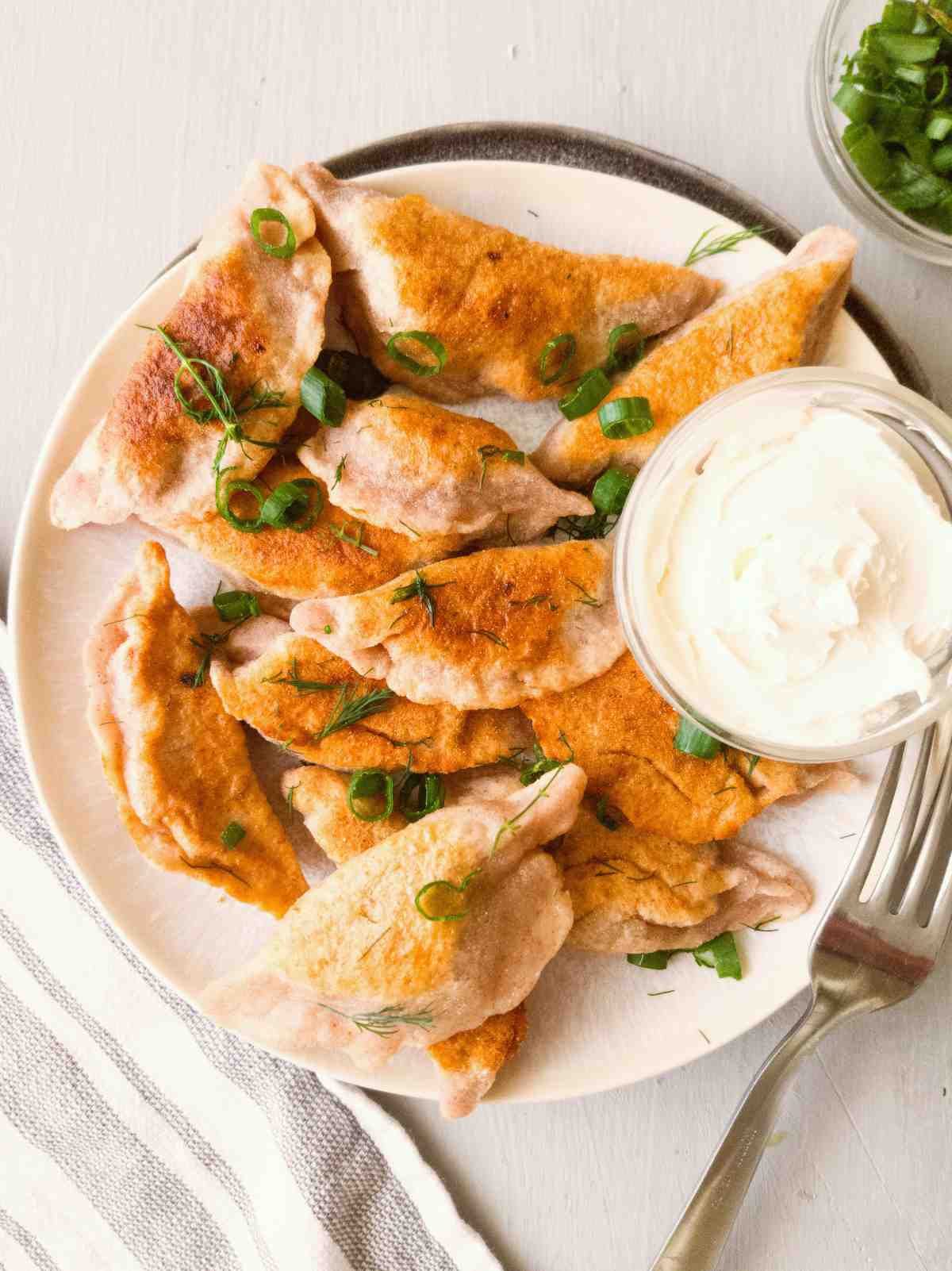 Gluten-free pierogi on a plate with white sauce next to it.