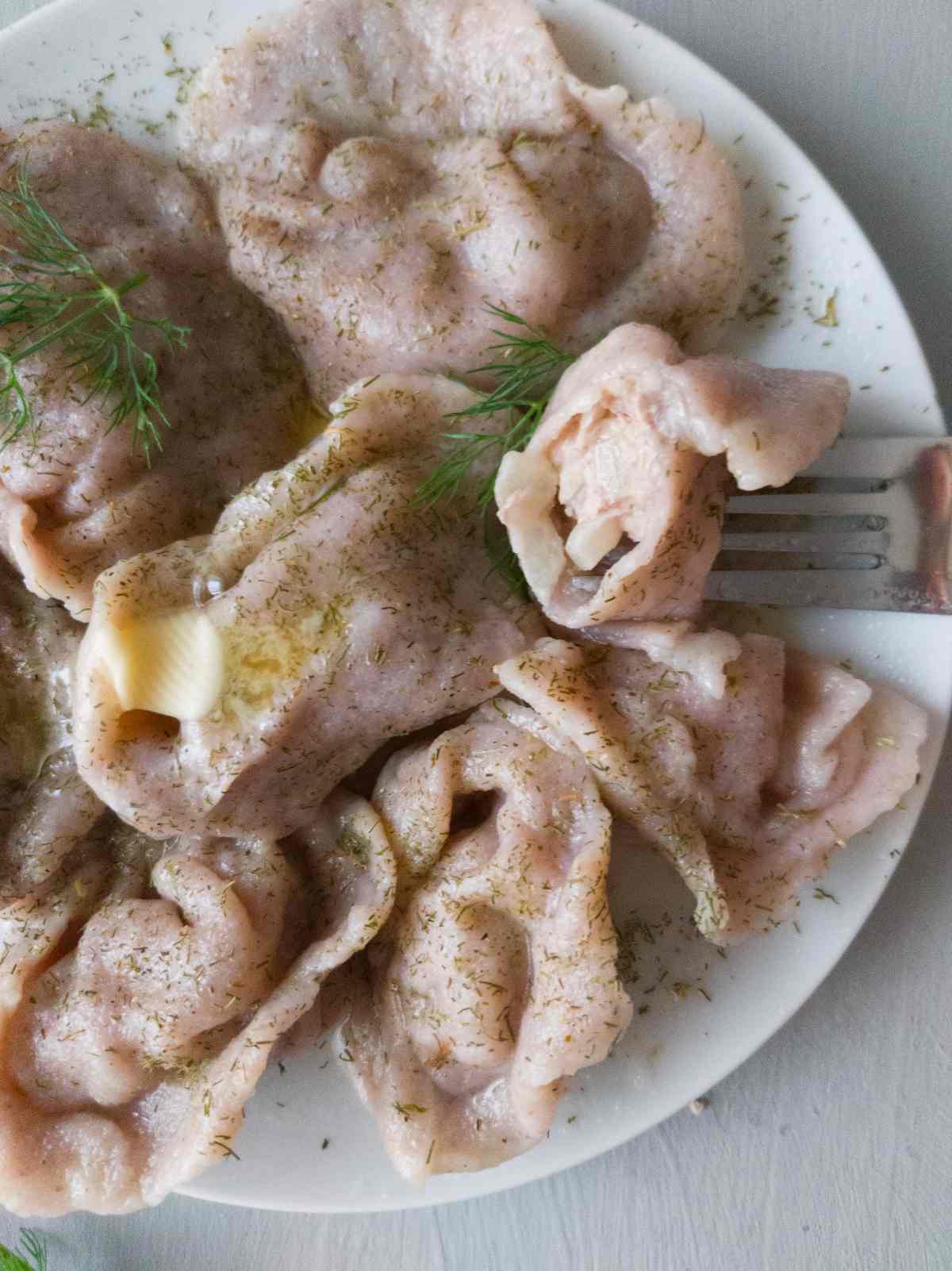 Pelmeni on a plate with a fork holding a dumpling that has been bitten into.