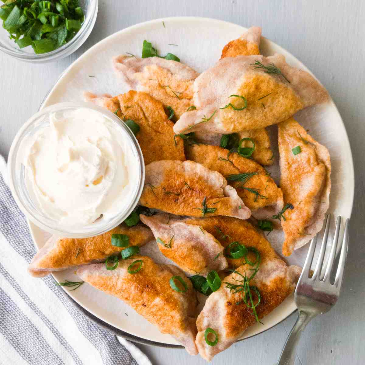 Fried gluten-free pierogies on a white plate with white sauce on the side.