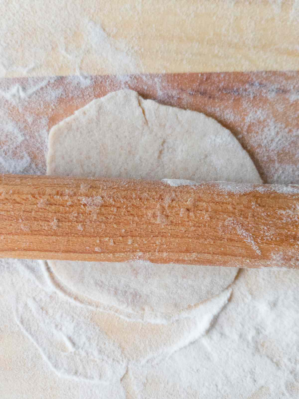 A little piece of dough rolled out with a wooden rolling pin that is laying on top of it.