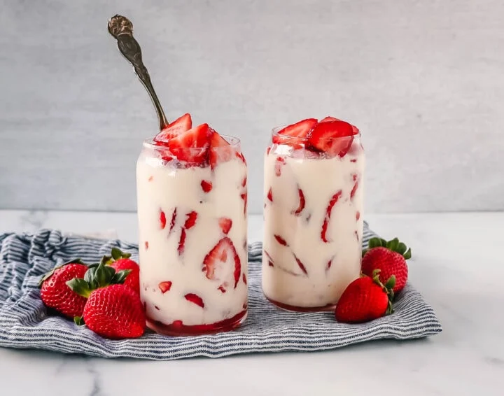 Two glasses filled with strawberries and cream with spoons sticking out.