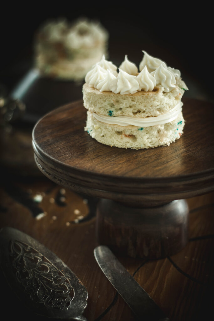 A mini cake on a dark wooden cake stand with a dark background.
