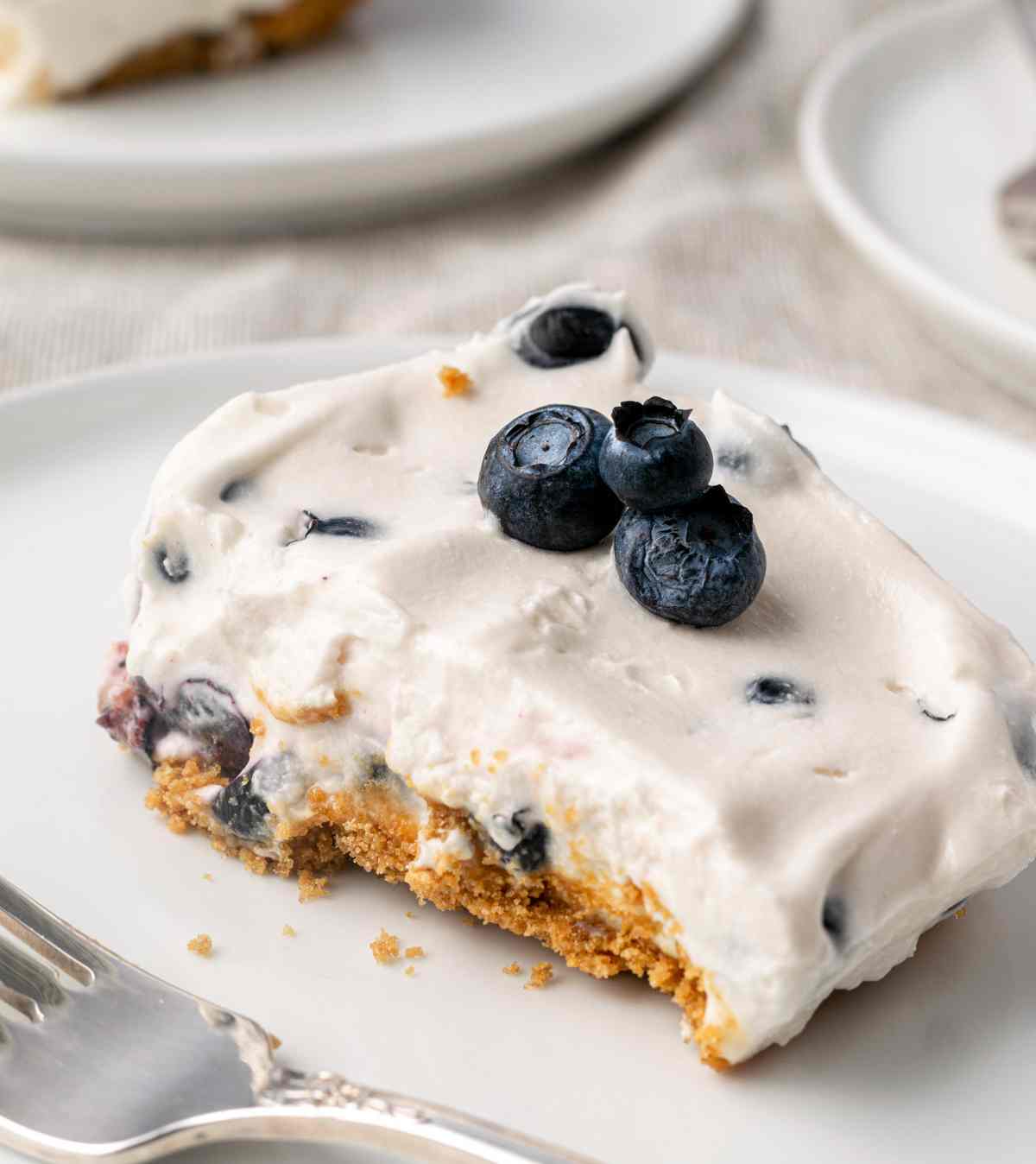 No bake blueberry cheesecake slice on a white plate with a fork next to it.