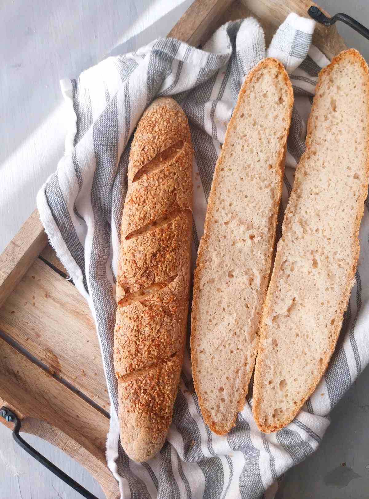 Gluten-free sourdough baguettes on a wooden tray with a kitchen towel. 