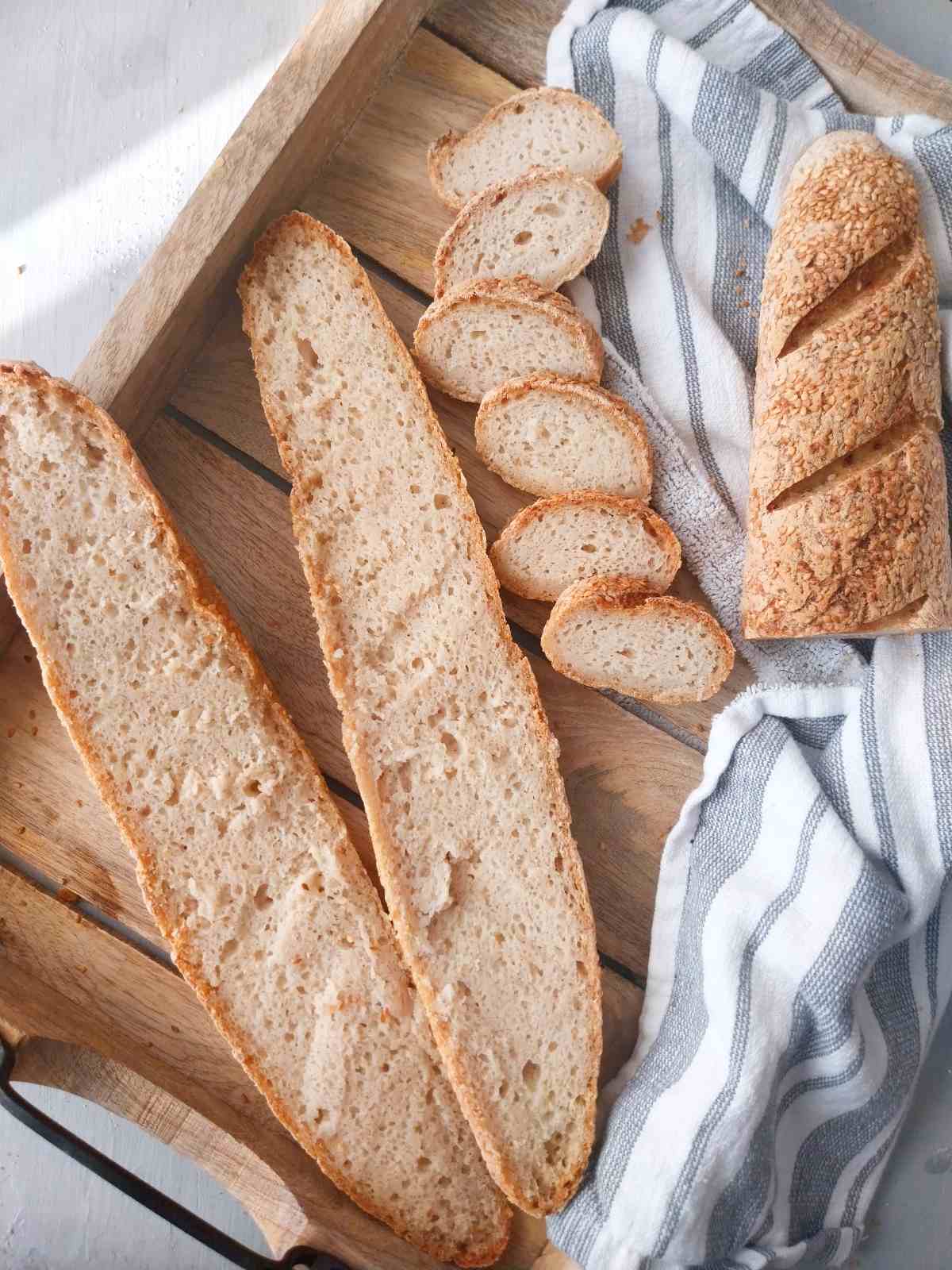Gluten-free sourdough French bread on a wooden tray sliced.