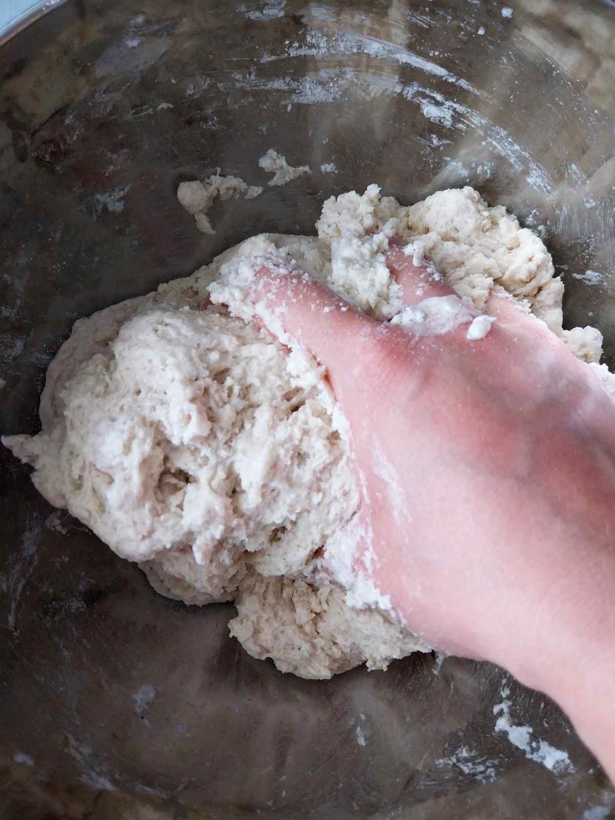 Kneading the dough by hand in a metal bowl.