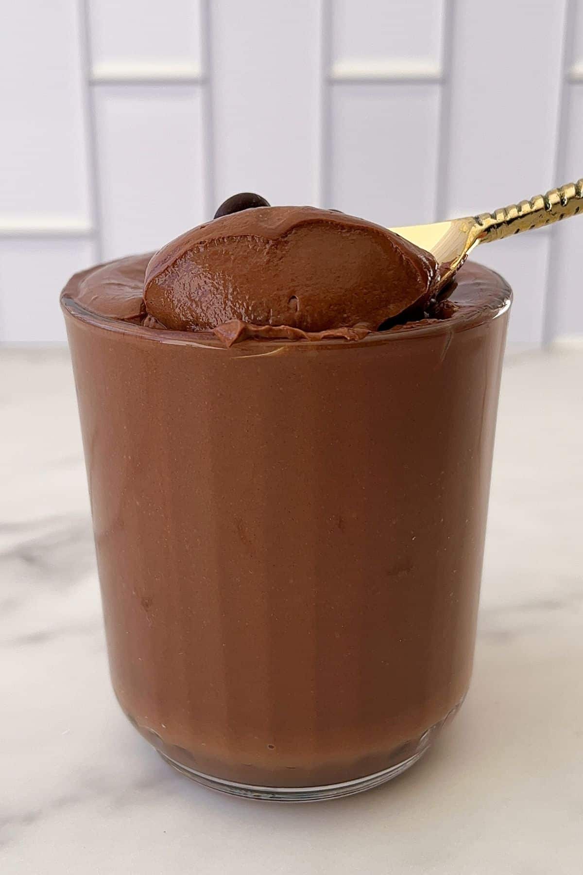 A glass filled with chocolate mousse with a golden spoon scooping some out.