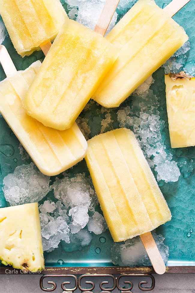 Pineapple popsicles on ice laying on a green surface.