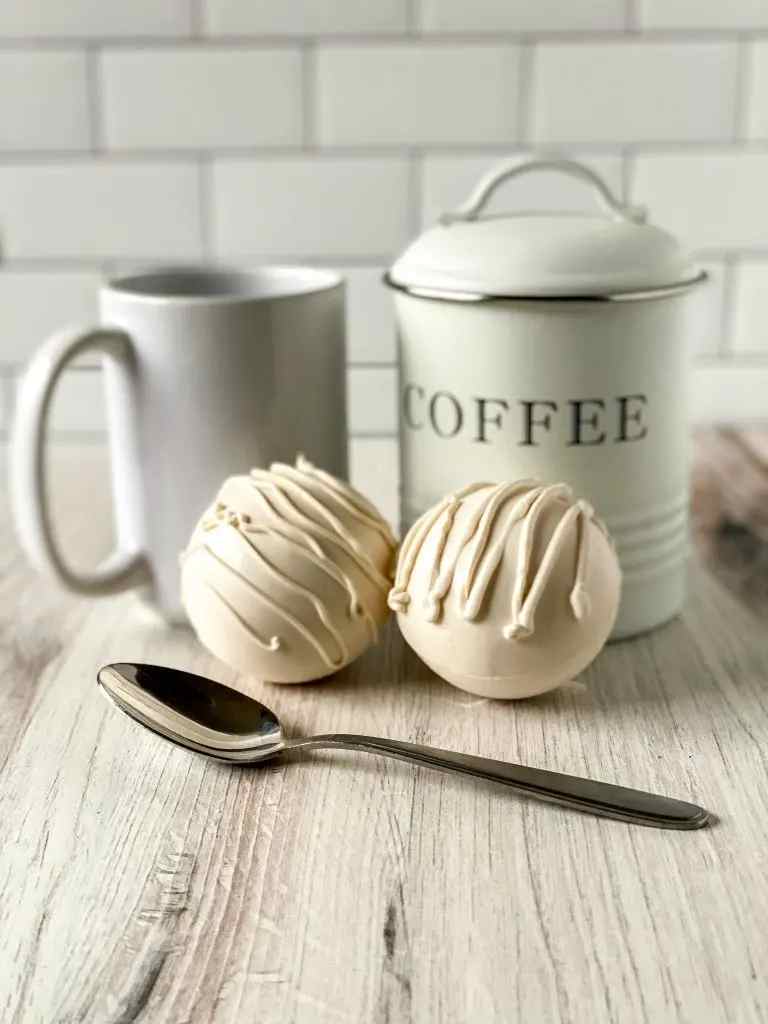 White chocolate coffee bombs with a cup and a coffee box in the background.