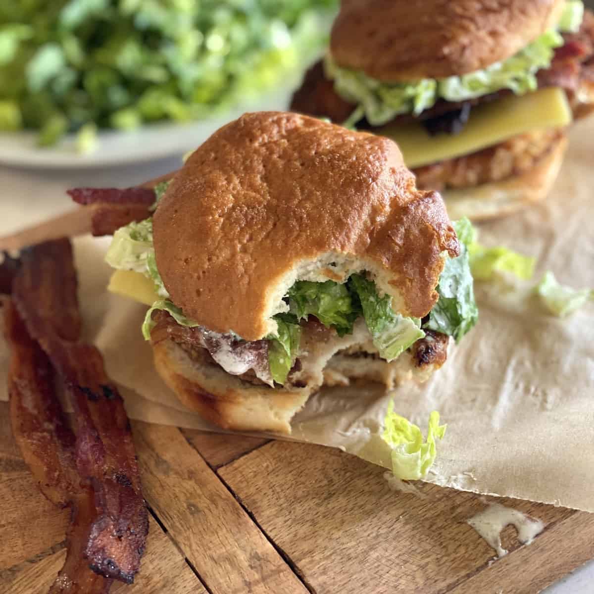 A burger bite with fried bacon on the side on a wooden board with a piece of parchment paper.