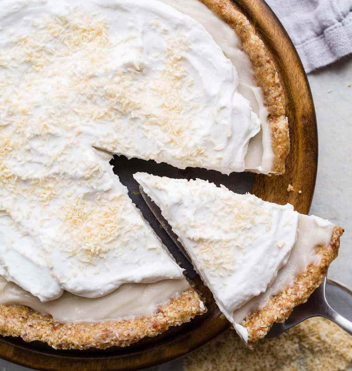 Coconut cream pie with a slice cut out and held by a metal spatula.