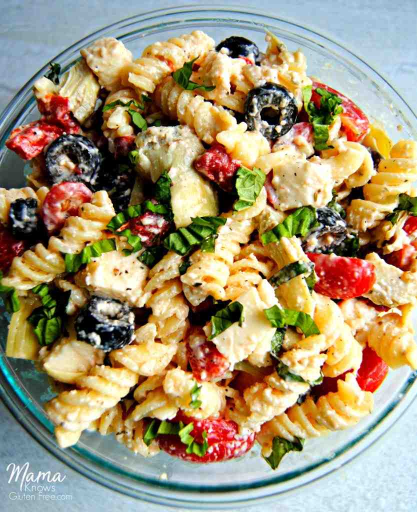 A bowl of pasta salad with olives and tomatoes flat lay.