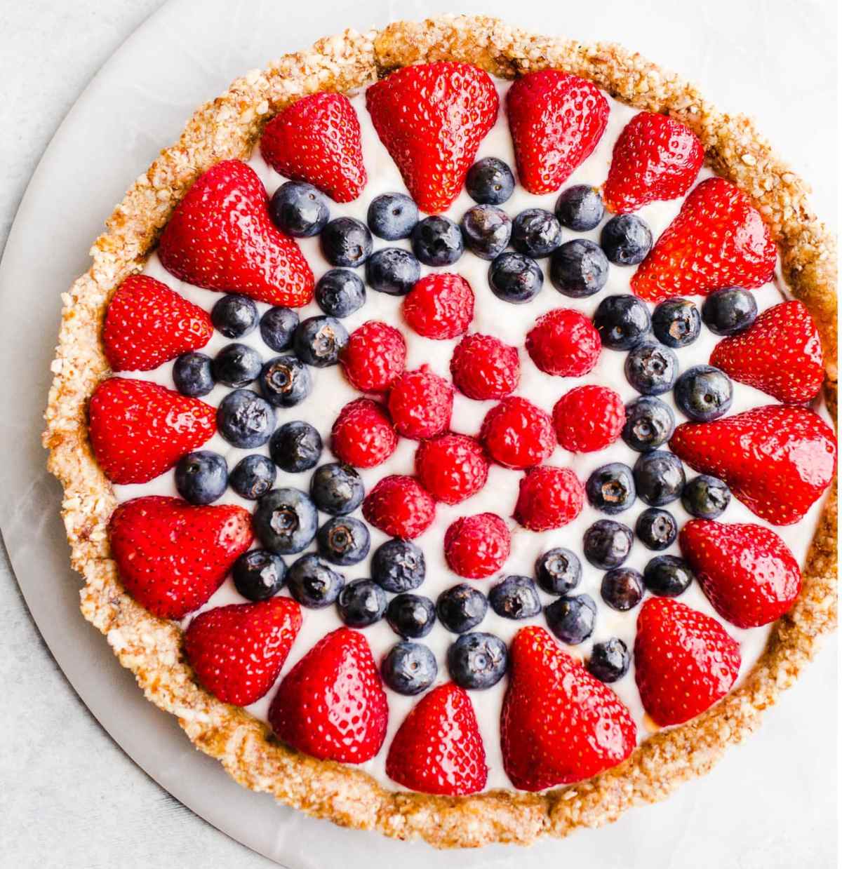 A round berry tart with fresh strawberries and blueberries on a white platter. 