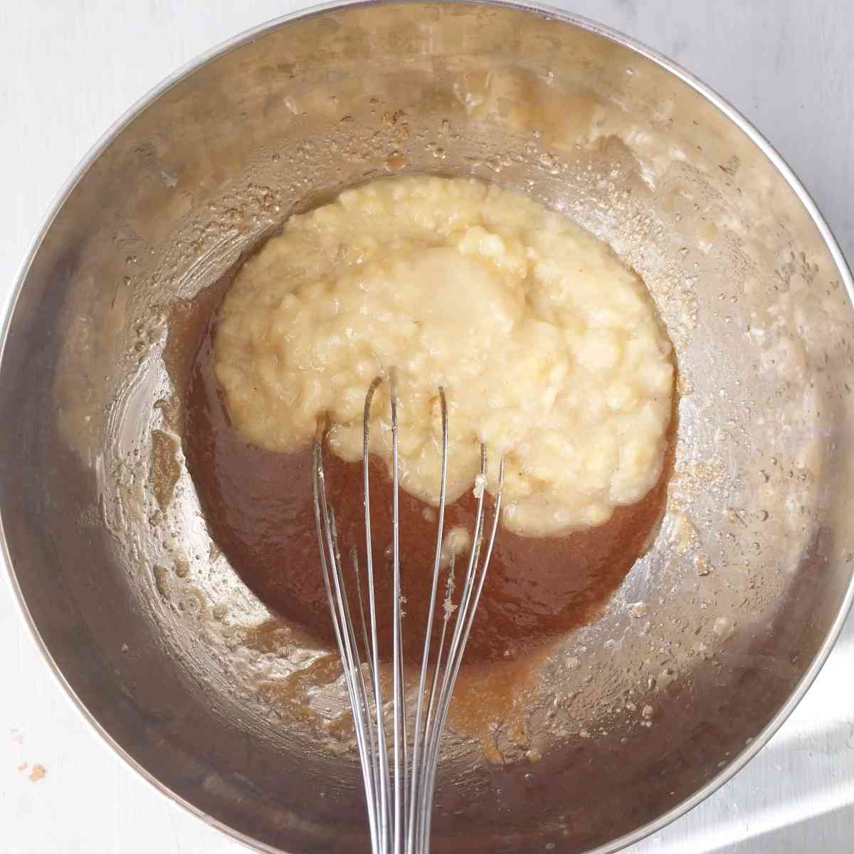 Mashed bananas with the sugar mix in a large metal bowl with a whisk.