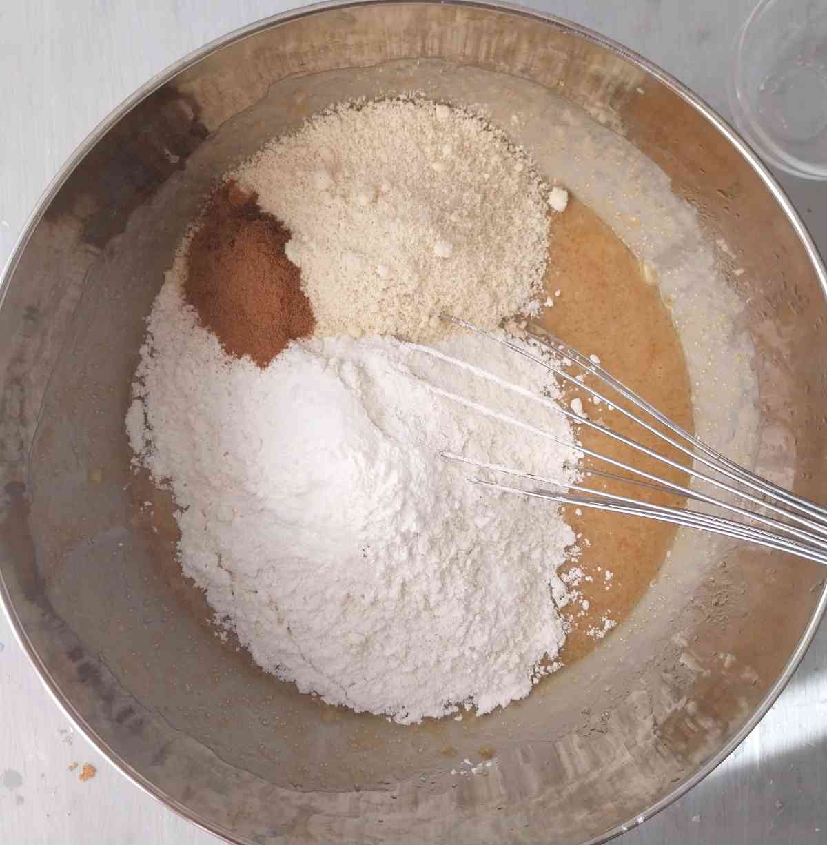 A metal bowl with dry and wet ingredients and a whisk.