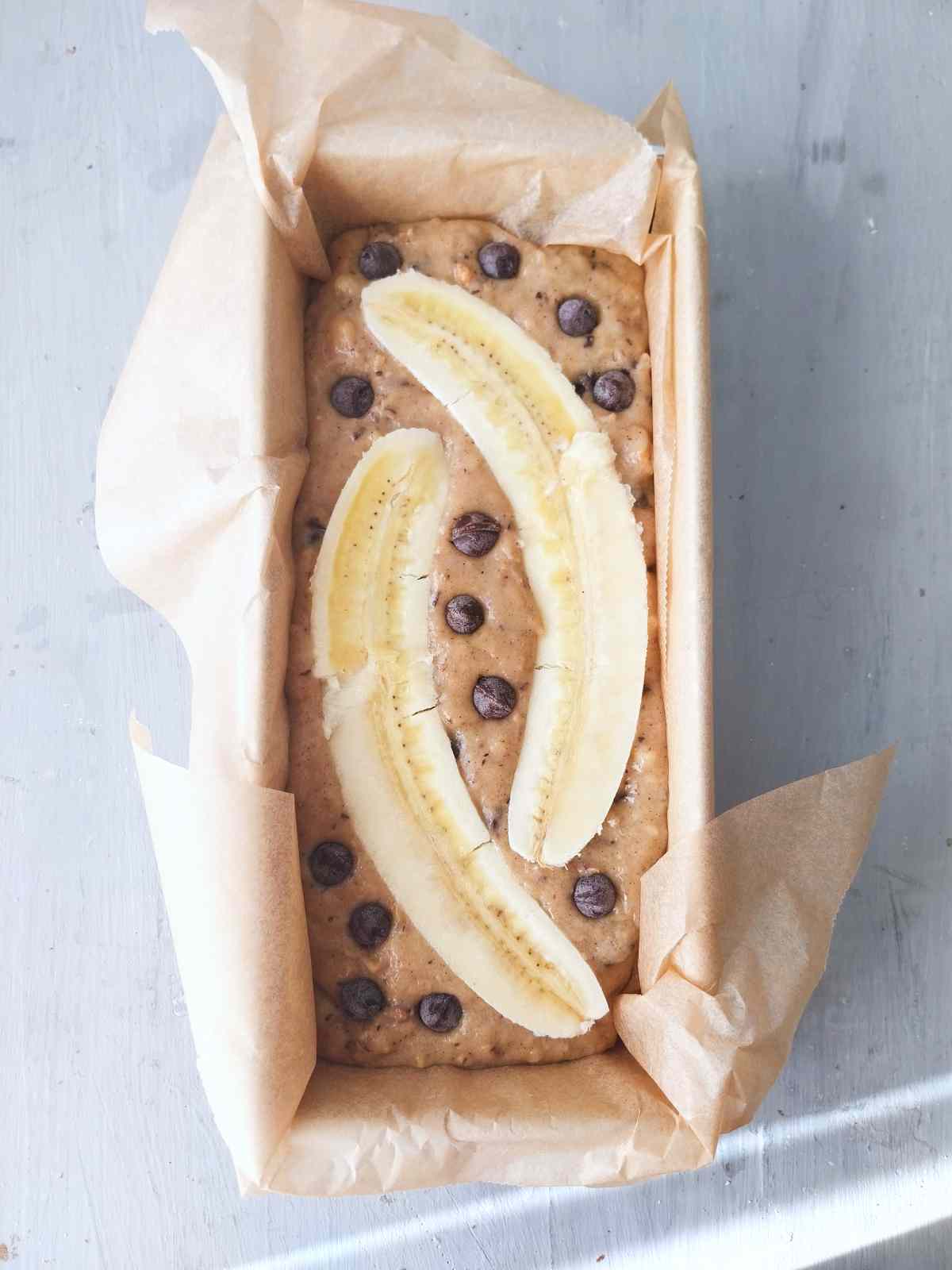 Banana bread batter in the bread pan with banana slices and chocolate chips on top. 